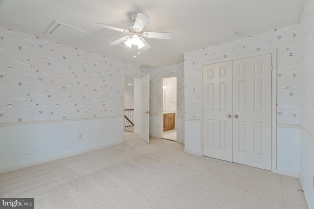 unfurnished bedroom with a closet, a wainscoted wall, light carpet, attic access, and wallpapered walls