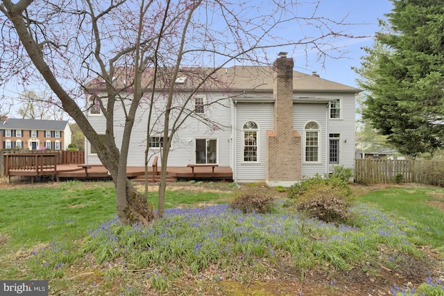 back of property with a yard, fence, a deck, and a chimney