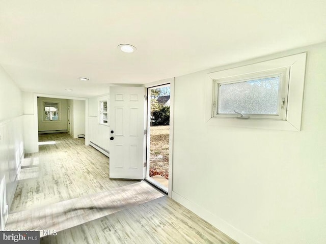 hallway with a wealth of natural light, light hardwood / wood-style floors, and a baseboard heating unit