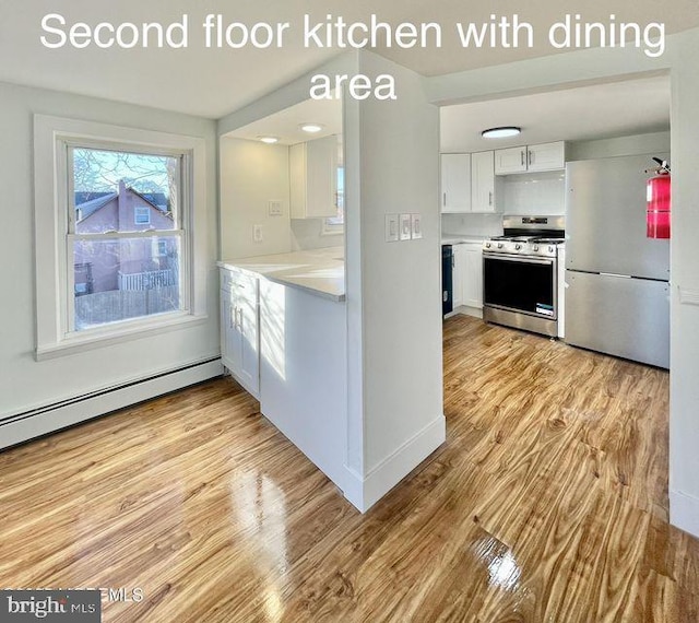 kitchen featuring white cabinets, appliances with stainless steel finishes, baseboard heating, and light hardwood / wood-style flooring