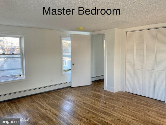 unfurnished bedroom with hardwood / wood-style floors, baseboard heating, a closet, and a textured ceiling