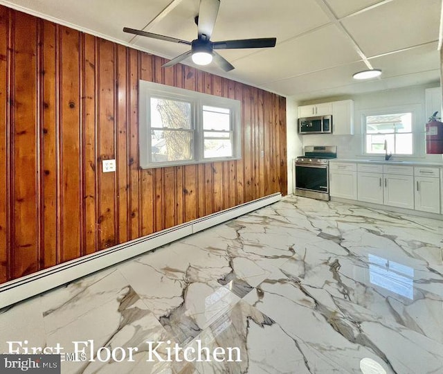 interior space featuring stainless steel appliances, sink, a baseboard heating unit, white cabinets, and wooden walls