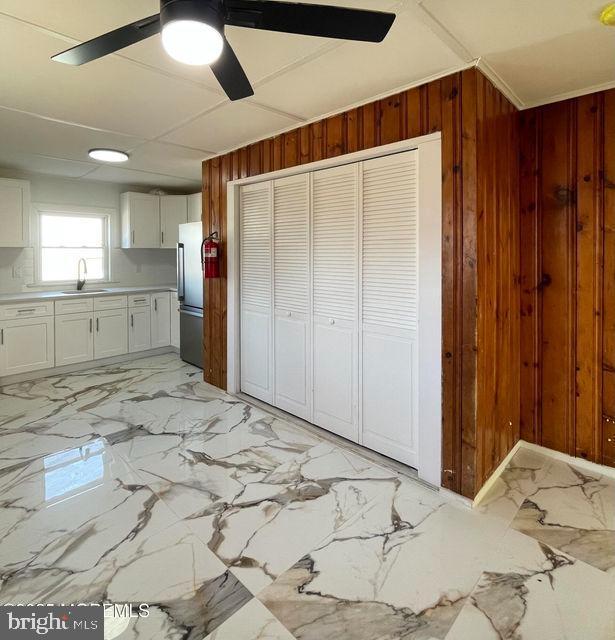 kitchen featuring ceiling fan, stainless steel refrigerator, wood walls, sink, and white cabinetry