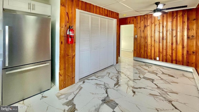 kitchen with ceiling fan, white cabinets, stainless steel fridge, and wooden walls