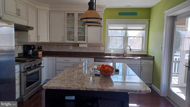 kitchen featuring a kitchen island, light stone countertops, stainless steel appliances, under cabinet range hood, and a sink