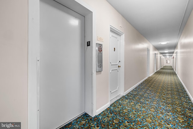 hall featuring baseboards, elevator, and carpet