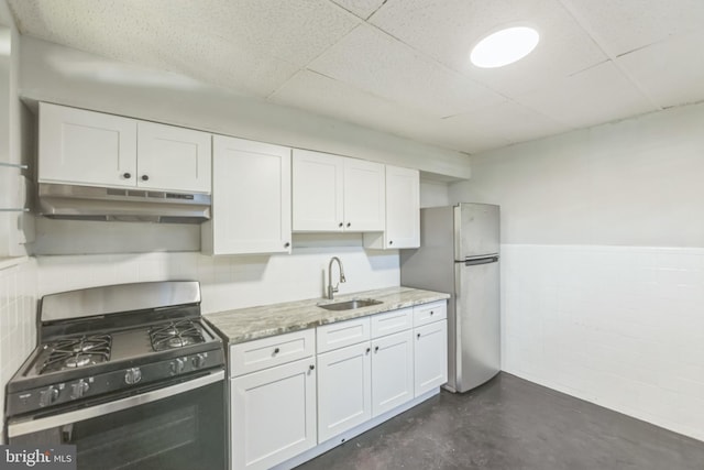 kitchen with sink, gas range, white cabinetry, stainless steel refrigerator, and light stone countertops