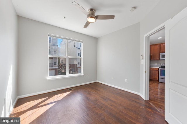 spare room with a ceiling fan, dark wood-style flooring, visible vents, and baseboards