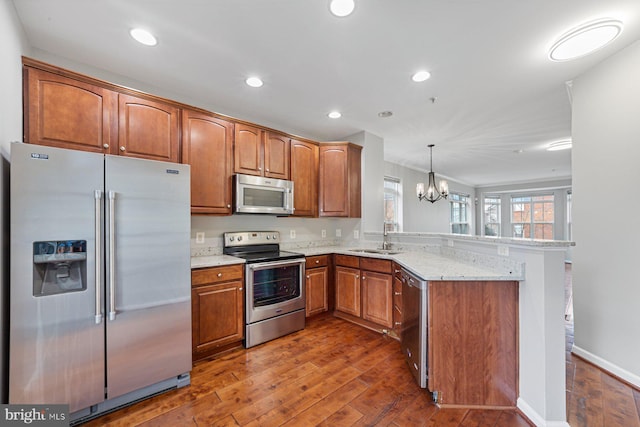 kitchen with hardwood / wood-style flooring, a peninsula, a sink, appliances with stainless steel finishes, and brown cabinets