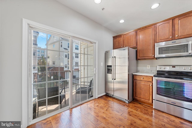 kitchen featuring stainless steel appliances, recessed lighting, light countertops, light wood-style flooring, and brown cabinetry