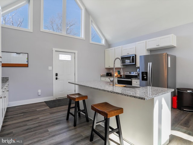 kitchen featuring appliances with stainless steel finishes, a center island with sink, a breakfast bar area, light stone countertops, and white cabinets