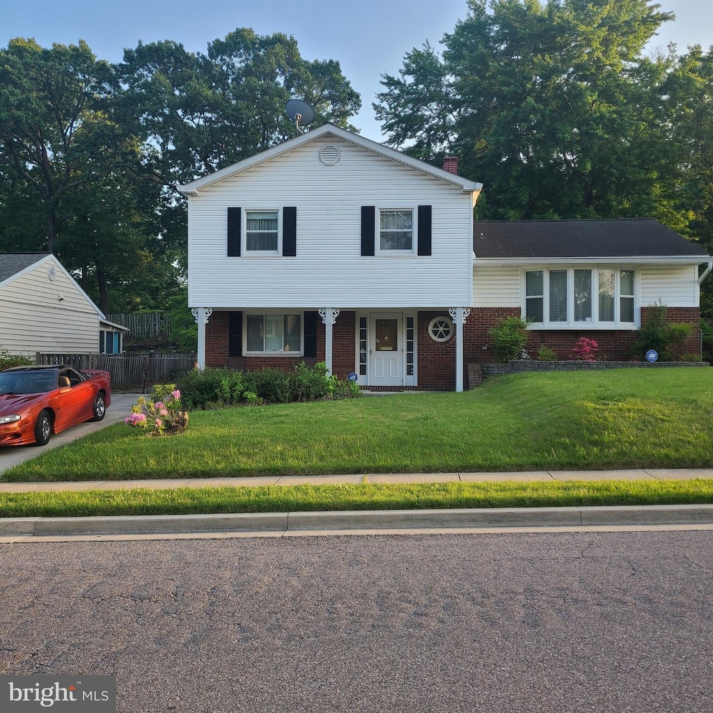 view of front of home featuring a front yard, brick siding, fence, and a chimney