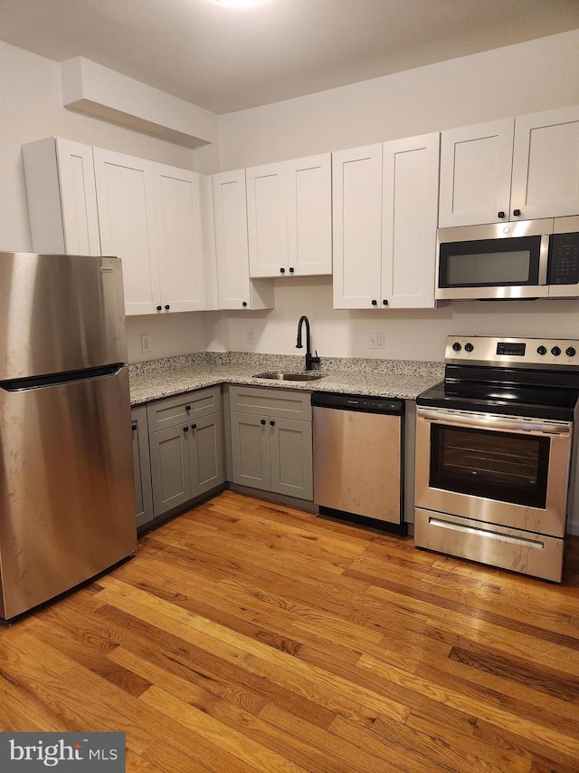 kitchen featuring sink, gray cabinets, appliances with stainless steel finishes, white cabinets, and light wood-type flooring