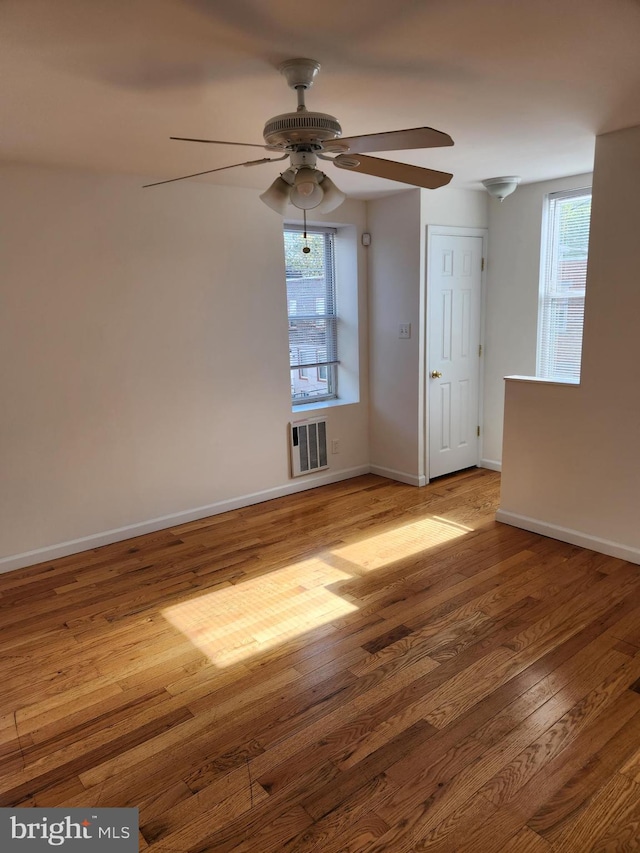 spare room with heating unit, ceiling fan, hardwood / wood-style flooring, and a healthy amount of sunlight