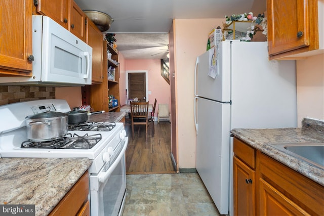 kitchen featuring sink, backsplash, white appliances, and light stone countertops