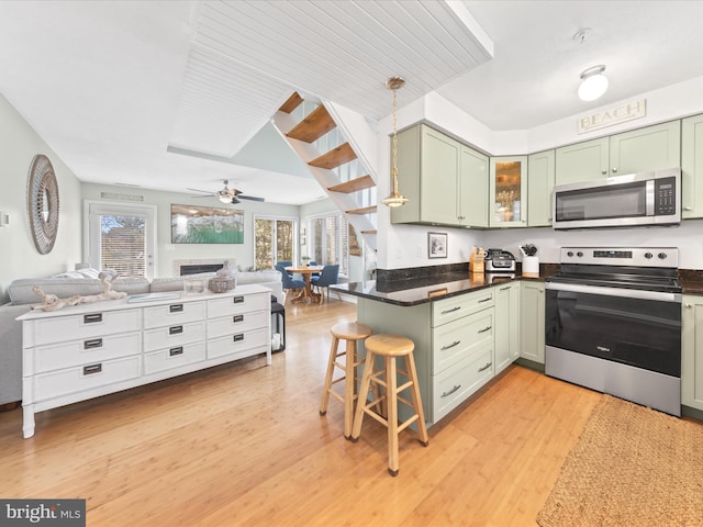 kitchen featuring stainless steel appliances, open floor plan, light wood-style floors, and green cabinets