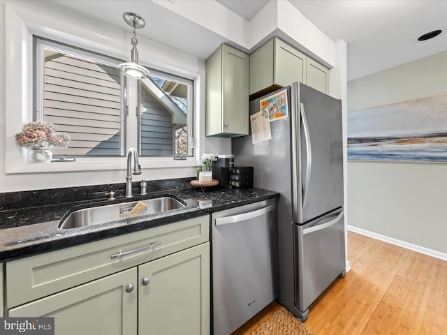 kitchen with light wood-style flooring, stainless steel appliances, a sink, green cabinets, and dark stone countertops