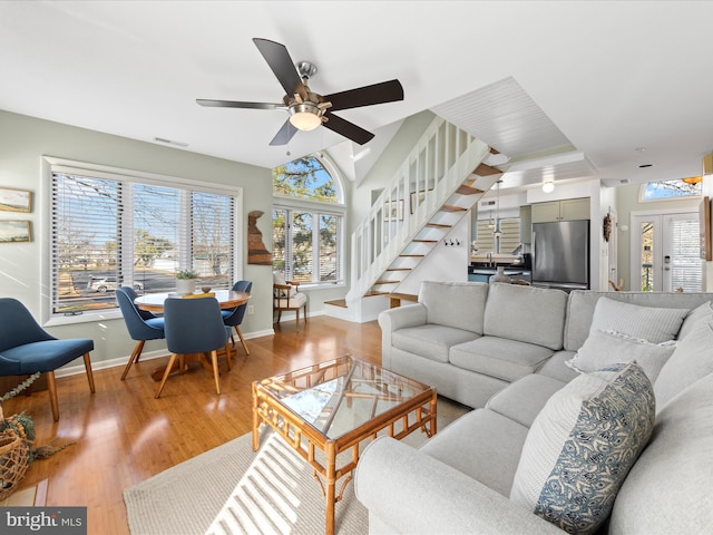 living area with baseboards, ceiling fan, wood finished floors, stairs, and vaulted ceiling