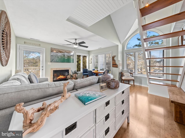 living area with light wood-style flooring, vaulted ceiling, ceiling fan, and a tile fireplace