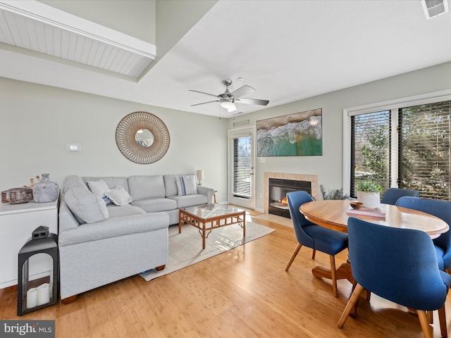 living area with a fireplace with flush hearth, wood finished floors, visible vents, and a ceiling fan