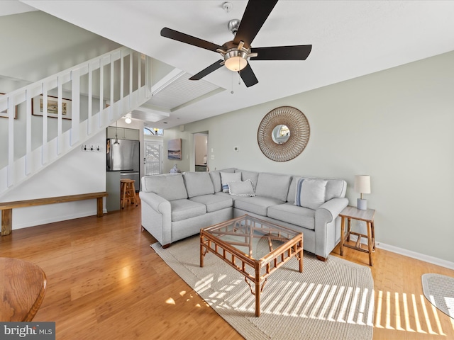 living room featuring wood finished floors, ceiling fan, baseboards, and stairs