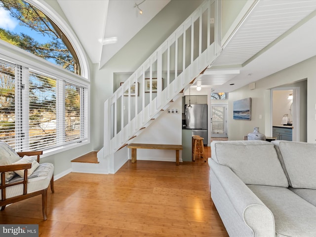 living room with high vaulted ceiling, baseboards, stairway, and light wood finished floors