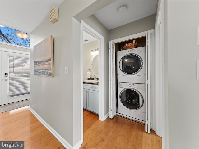 laundry room featuring laundry area, a sink, baseboards, light wood-style floors, and stacked washing maching and dryer