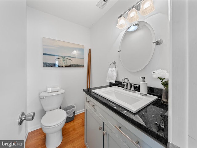 half bathroom featuring baseboards, visible vents, toilet, wood finished floors, and vanity