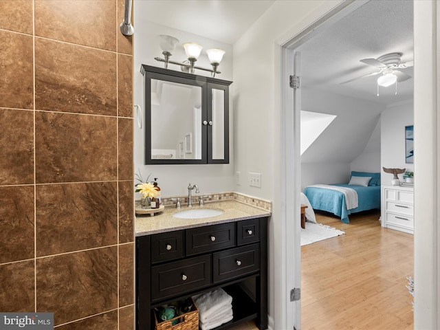 ensuite bathroom featuring lofted ceiling, ensuite bath, ceiling fan, wood finished floors, and vanity