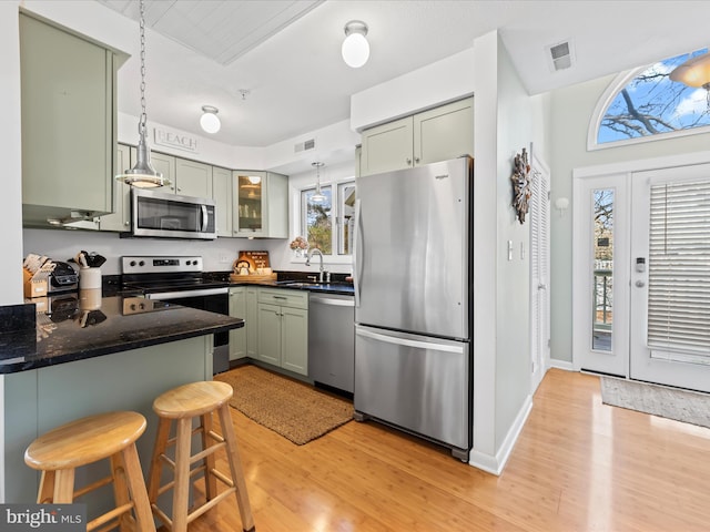 kitchen with visible vents, appliances with stainless steel finishes, a peninsula, a kitchen bar, and green cabinetry