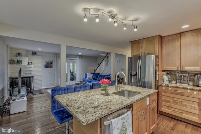 kitchen with a sink, stainless steel appliances, open floor plan, a brick fireplace, and an island with sink