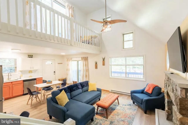 living room with a healthy amount of sunlight, a baseboard heating unit, sink, and light wood-type flooring