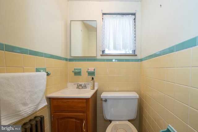 half bathroom with tile walls, toilet, vanity, and radiator heating unit