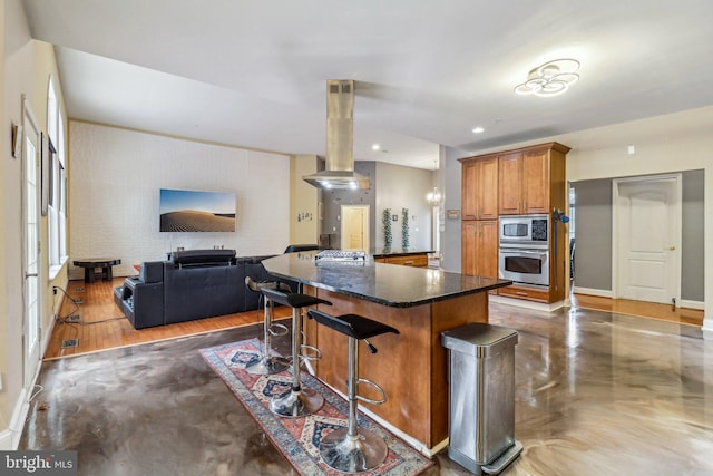 kitchen featuring island range hood, appliances with stainless steel finishes, brown cabinets, open floor plan, and a breakfast bar area