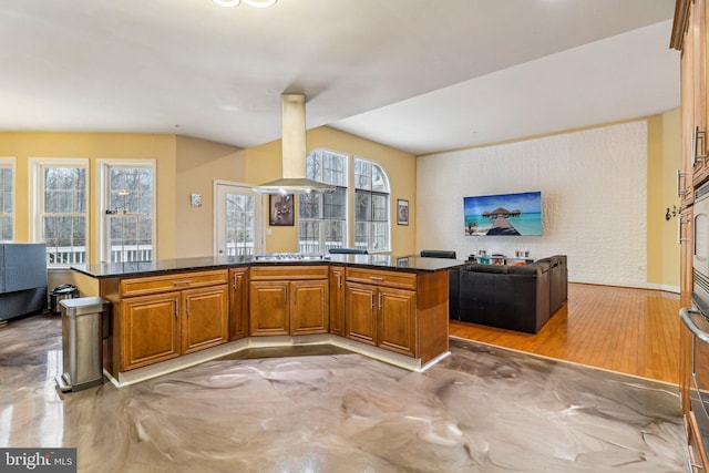 kitchen with open floor plan, a peninsula, brown cabinets, and island range hood