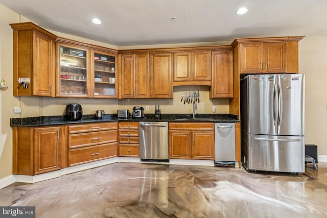 kitchen with dark stone counters, appliances with stainless steel finishes, a sink, and glass insert cabinets