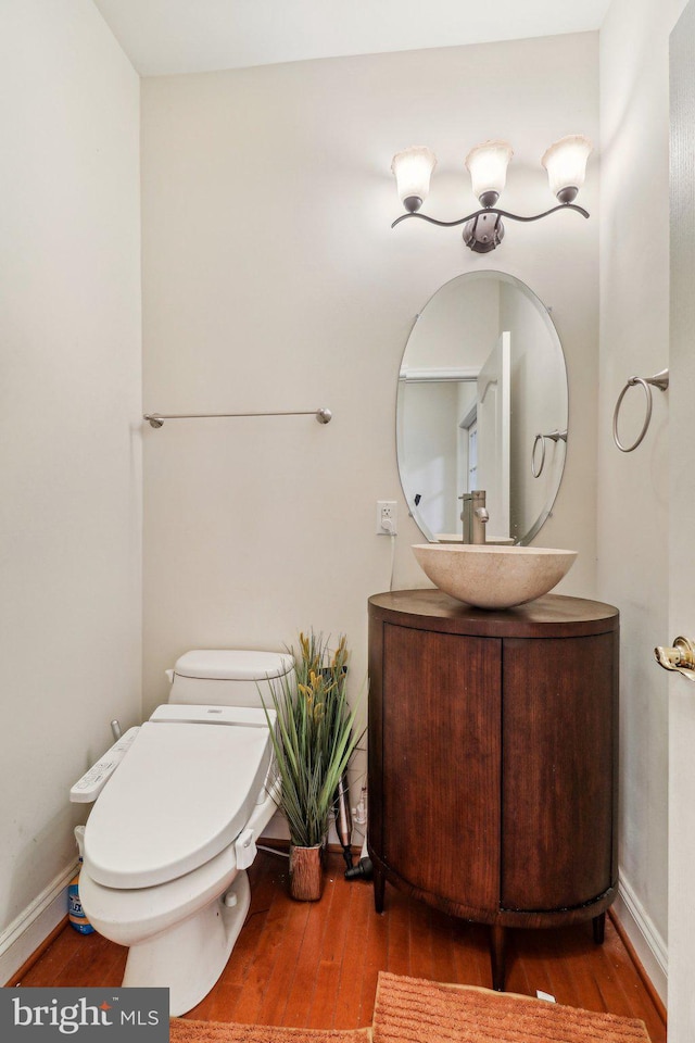 half bathroom with baseboards, vanity, toilet, and wood finished floors