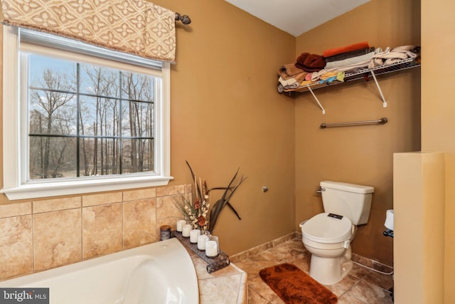 bathroom with tiled tub, tile patterned flooring, toilet, and baseboards