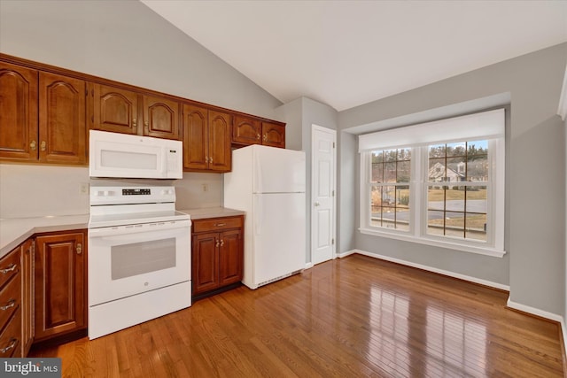 kitchen with brown cabinets, light countertops, vaulted ceiling, light wood-type flooring, and white appliances