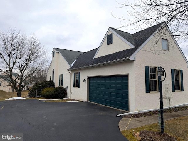 view of home's exterior with a garage, stucco siding, roof with shingles, and aphalt driveway