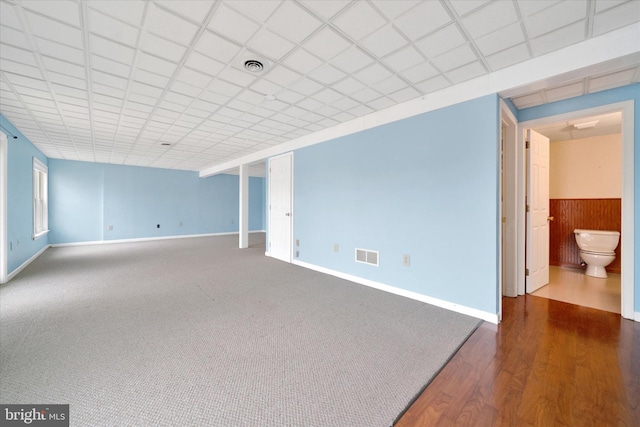 empty room with baseboards, visible vents, dark wood finished floors, and a drop ceiling