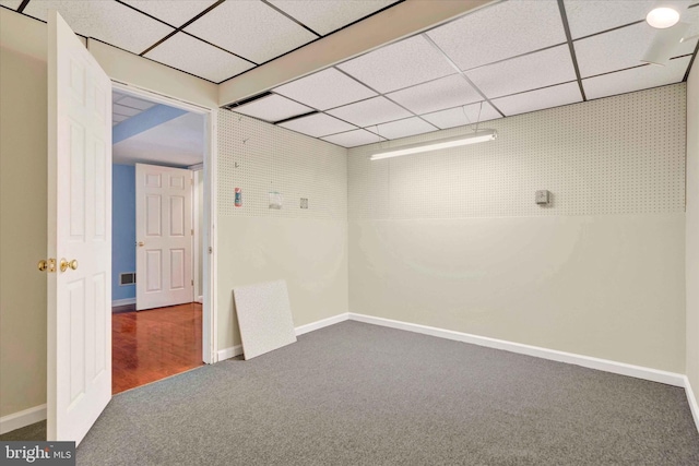 unfurnished room with dark carpet, a drop ceiling, and baseboards