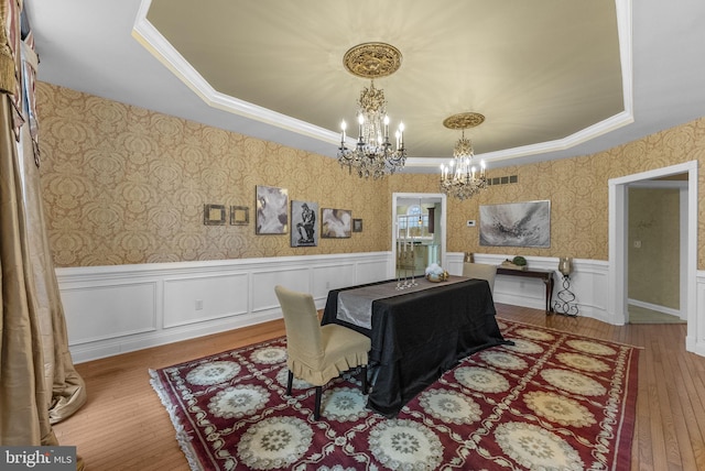 dining area with an inviting chandelier, crown molding, wood-type flooring, and a raised ceiling