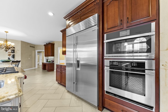 kitchen with stainless steel appliances, pendant lighting, a notable chandelier, and light stone counters