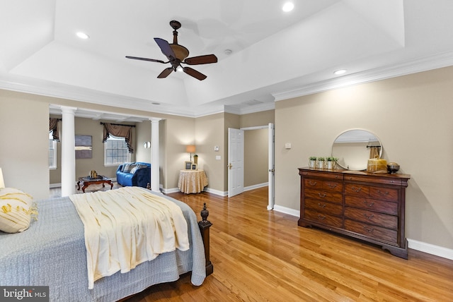 bedroom with a raised ceiling, ornamental molding, decorative columns, and light hardwood / wood-style floors