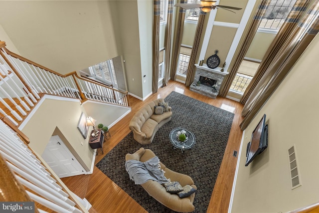 living room featuring hardwood / wood-style flooring, a fireplace, ceiling fan, and a high ceiling