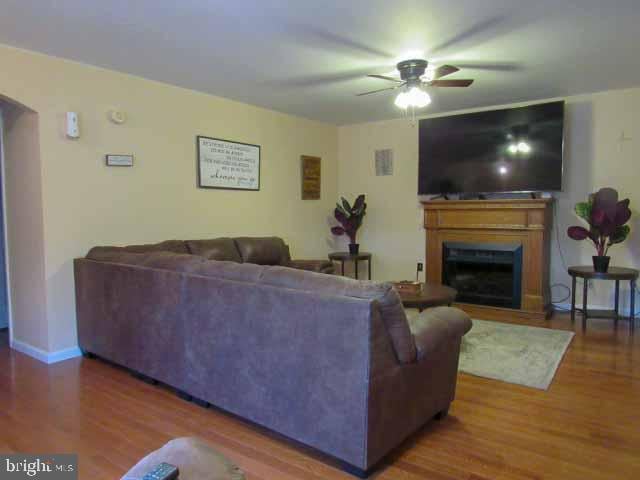 living room featuring a fireplace, wood finished floors, a ceiling fan, and baseboards