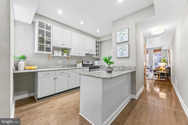 kitchen with light wood-style flooring, stainless steel range with gas cooktop, glass insert cabinets, and white cabinetry