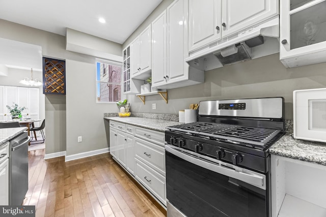 kitchen with under cabinet range hood, appliances with stainless steel finishes, glass insert cabinets, and white cabinets