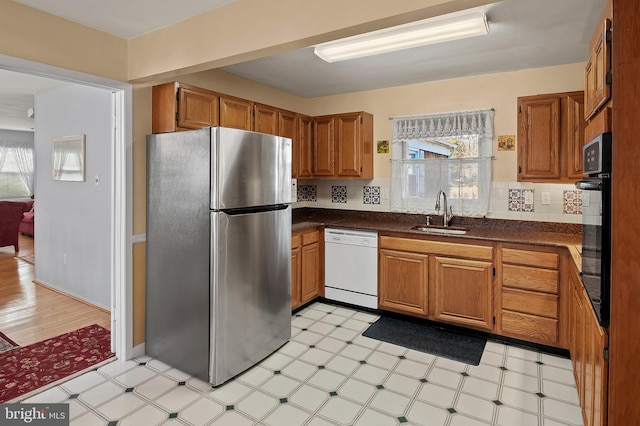 kitchen with dishwasher, dark countertops, freestanding refrigerator, light floors, and a sink